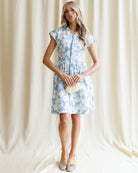 Woman wearing a blue floral dress against a white curtain background