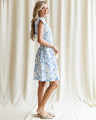 Woman wearing a blue floral dress standing against a white curtain