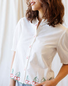 Woman wearing a white blouse with cherry embroidery on a plain background