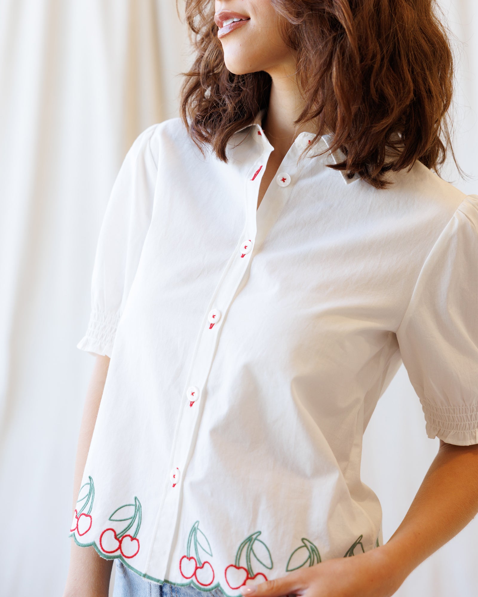 Woman wearing a white blouse with cherry embroidery on a plain background