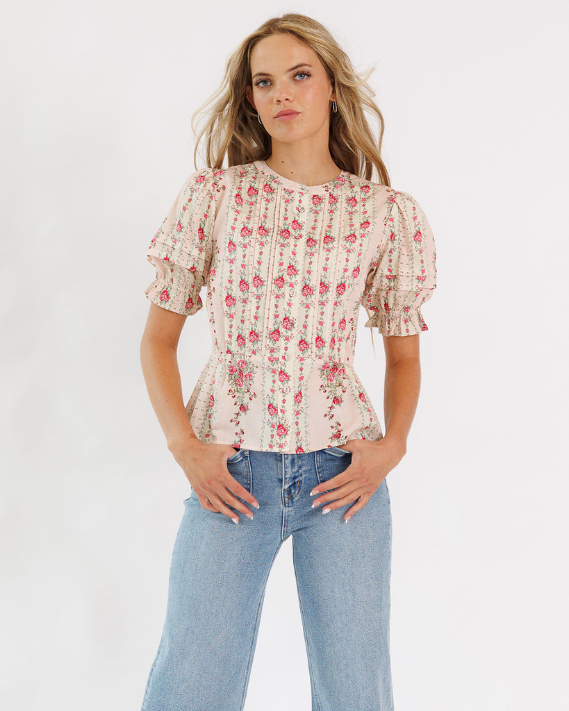 Model wearing a tan/pink with pink flower accents short sleeve blouse