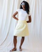 Woman wearing a white t-shirt and yellow skirt against a plain background