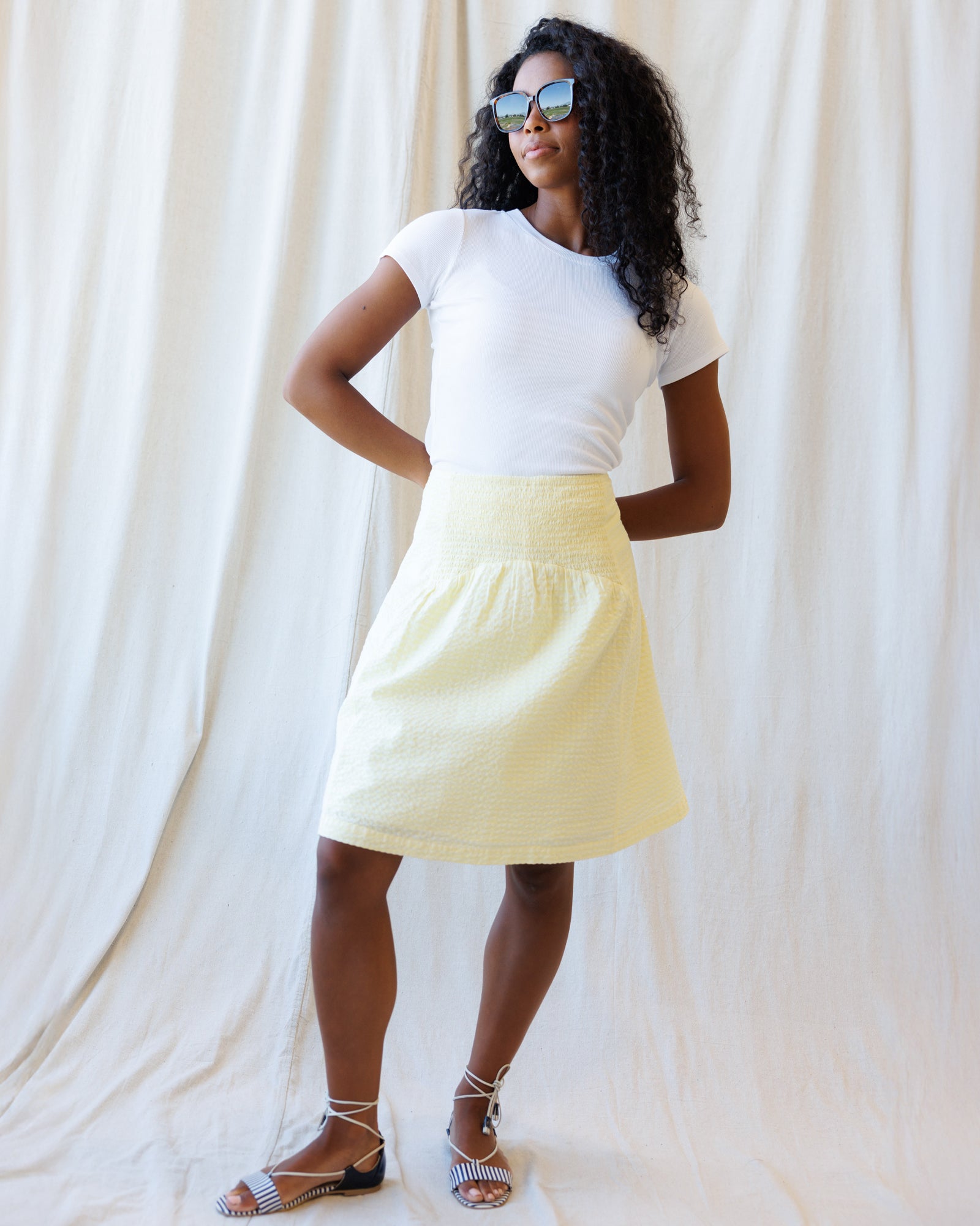 Woman wearing a white t-shirt and yellow skirt against a plain background