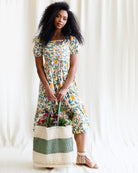 Woman wearing a floral dress holding a basket against a white curtain background
