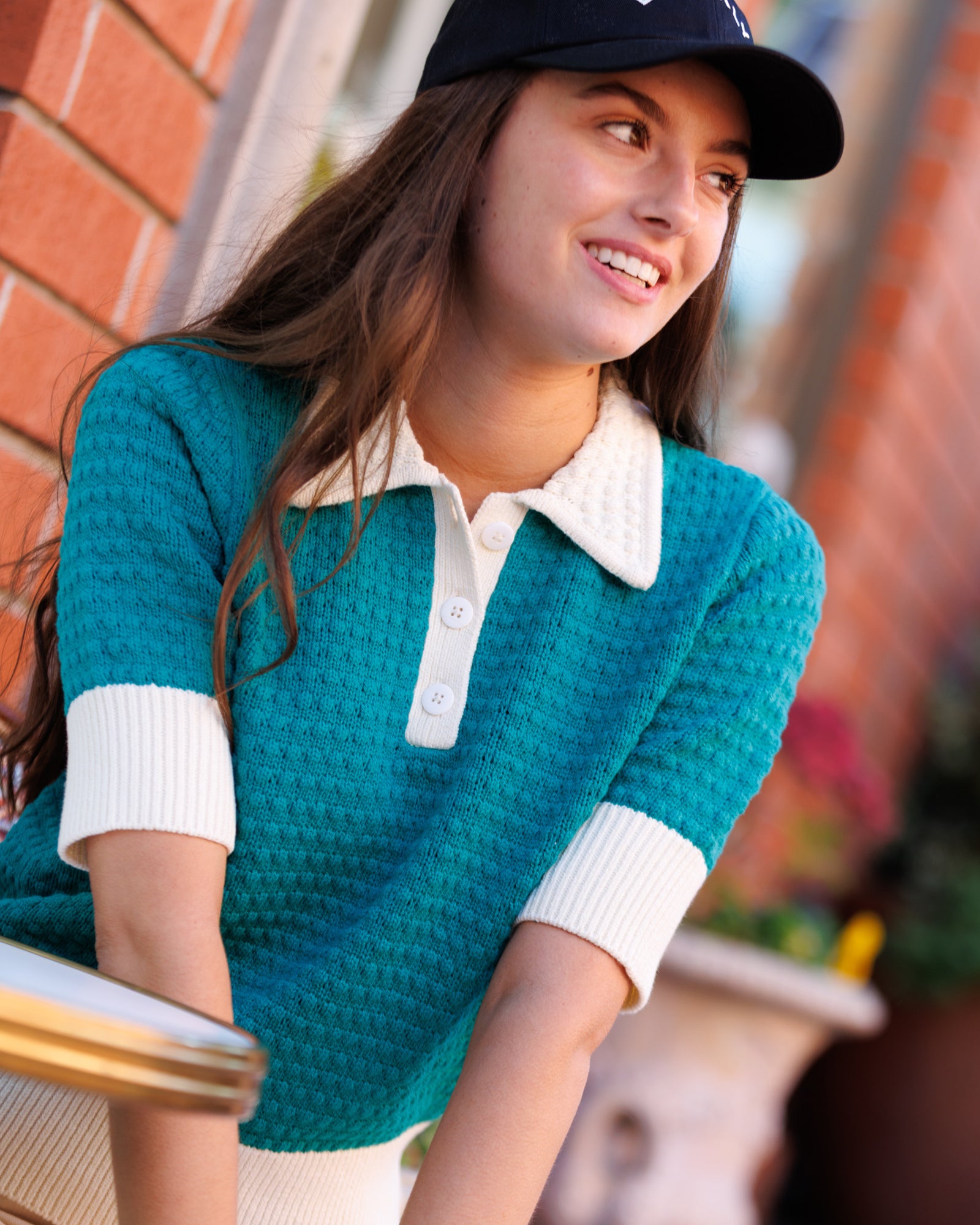 Woman wearing a teal sweater with white collar and cuffs, sitting outdoors.