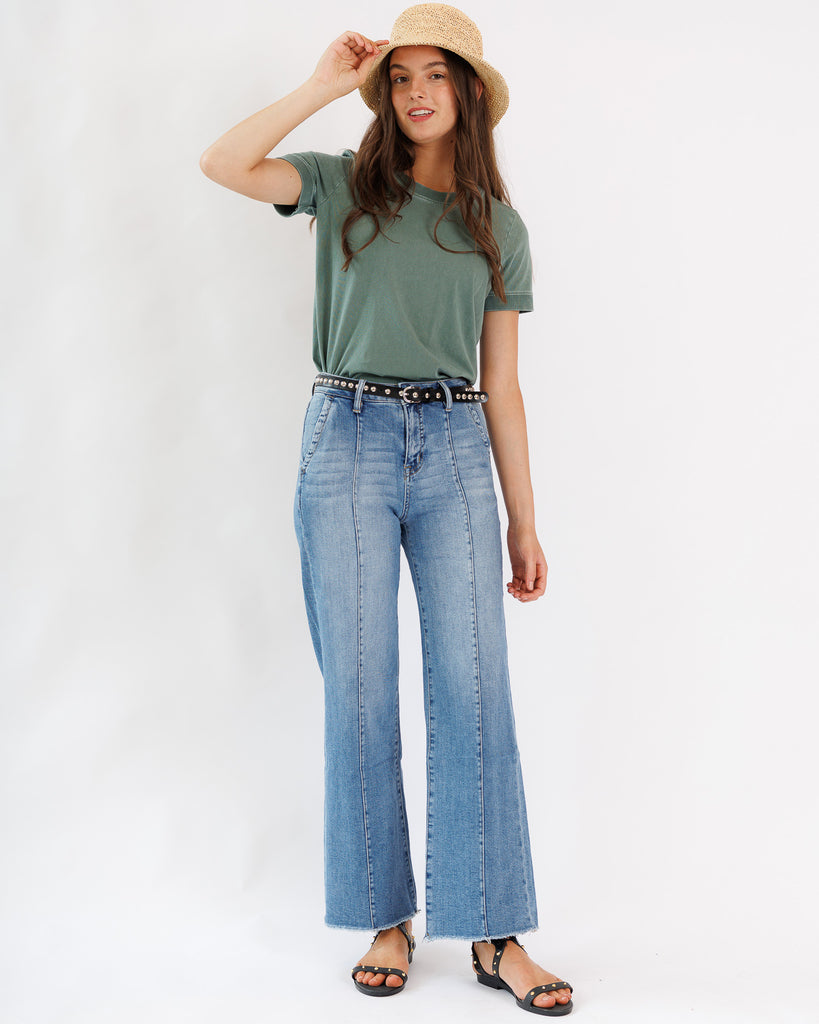 Woman wearing a green t-shirt and blue jeans with a beige hat on a white background