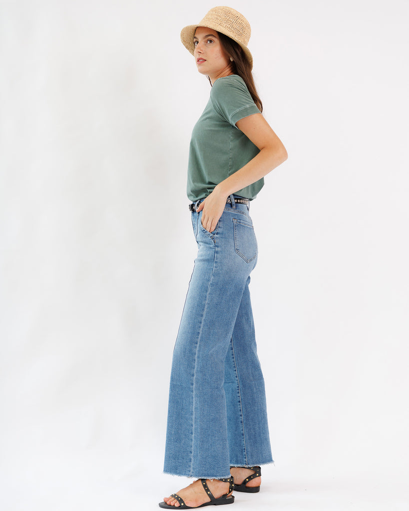 Woman wearing a green t-shirt and blue jeans with a white background
