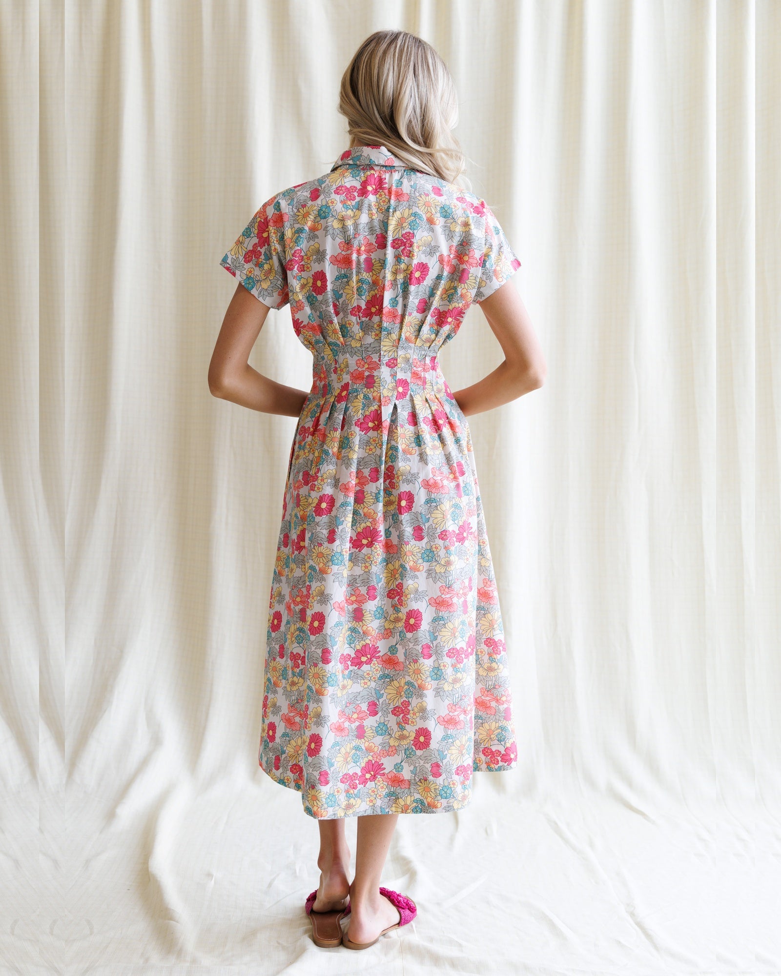 Woman wearing a floral dress against a white curtain background