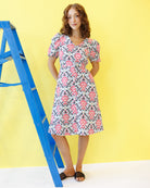 Woman wearing a floral dress standing next to a blue ladder against a yellow background