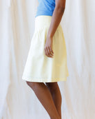 Person wearing a yellow skirt and blue top against a white curtain background