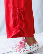 Person wearing red pants and white sneakers with cherry design on a light gray background