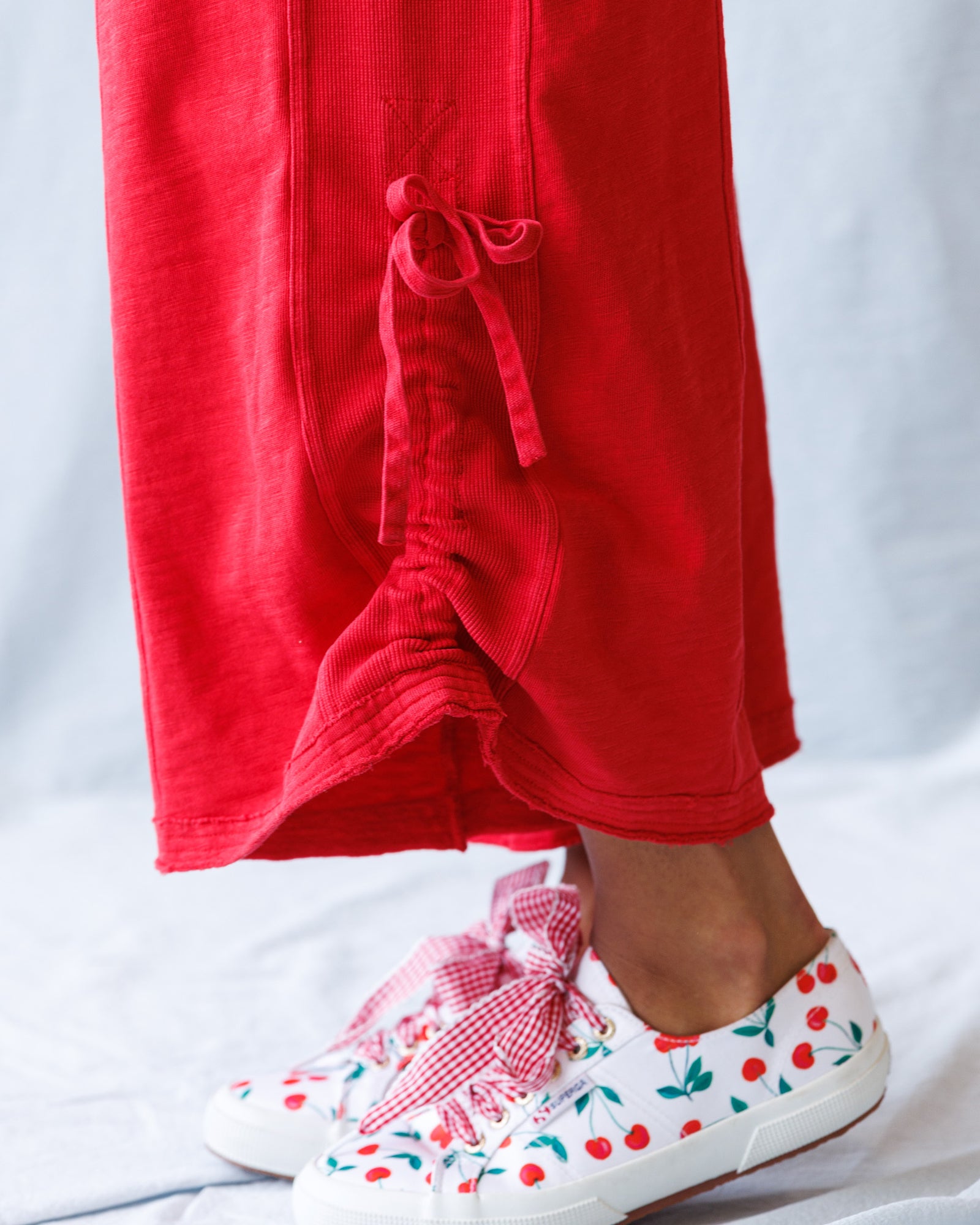 Person wearing red pants and white sneakers with cherry design on a light gray background