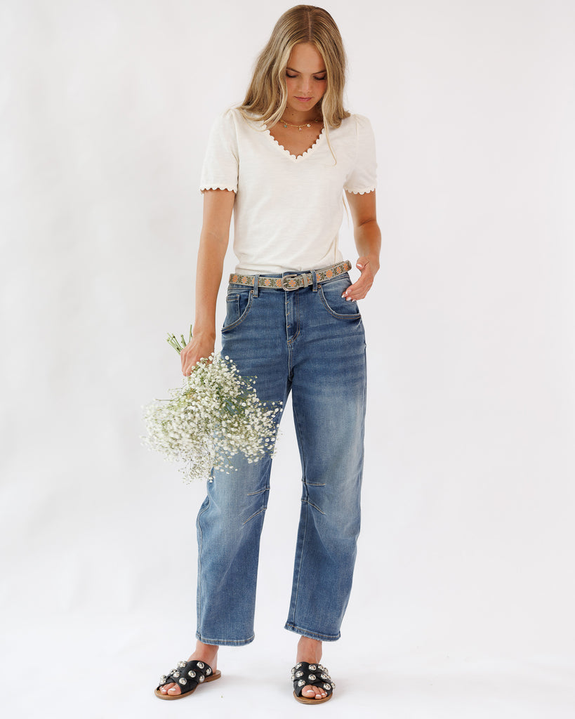Woman wearing a white top and blue jeans holding flowers on a white background