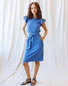 Woman wearing a blue polka dot dress against a white curtain background