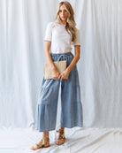 Woman wearing a white top and blue denim skirt holding a beige clutch against a white background