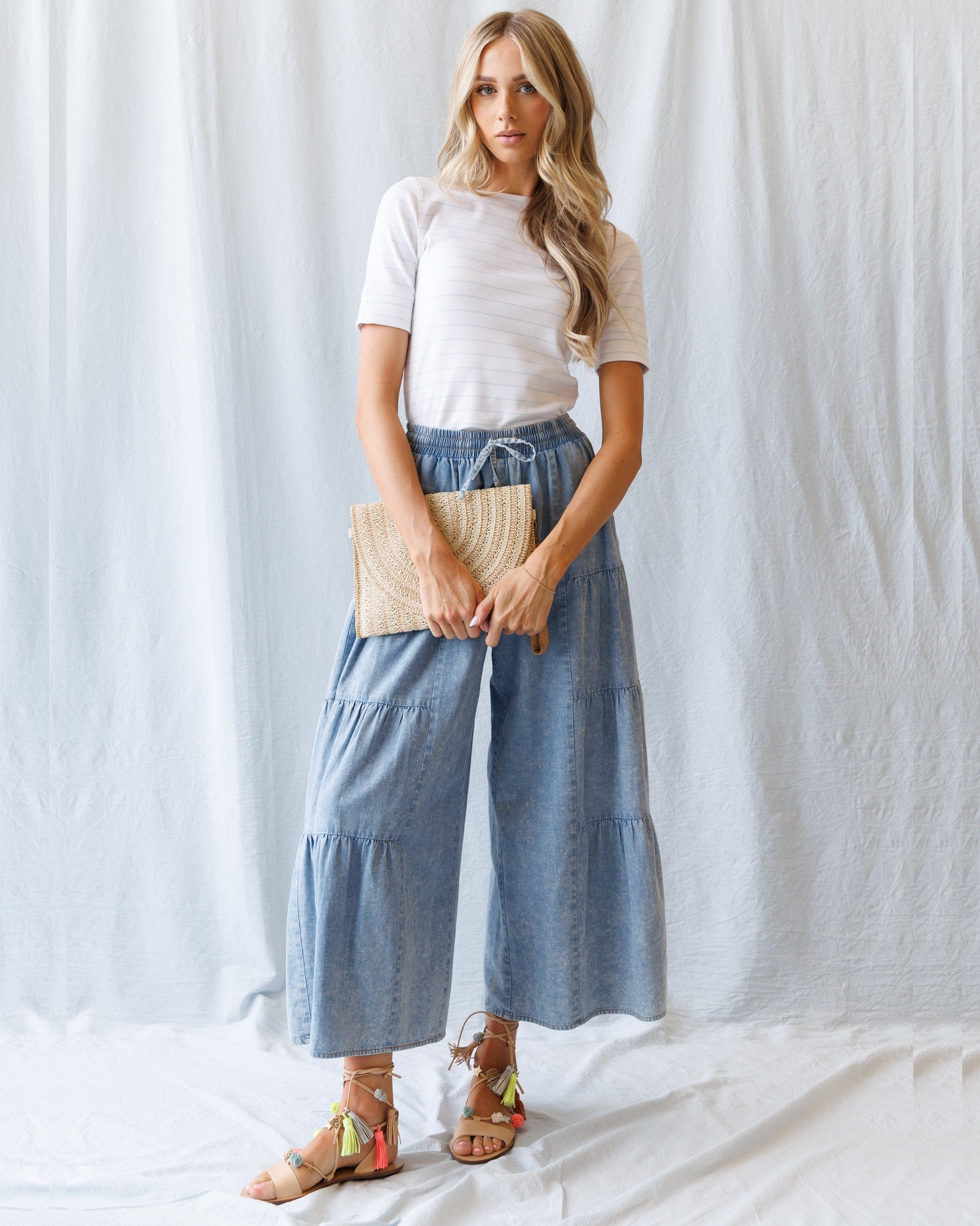 Woman wearing a white top and blue denim skirt holding a beige clutch against a white background