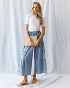 Woman standing wearing a white top and blue denim pants against a plain background