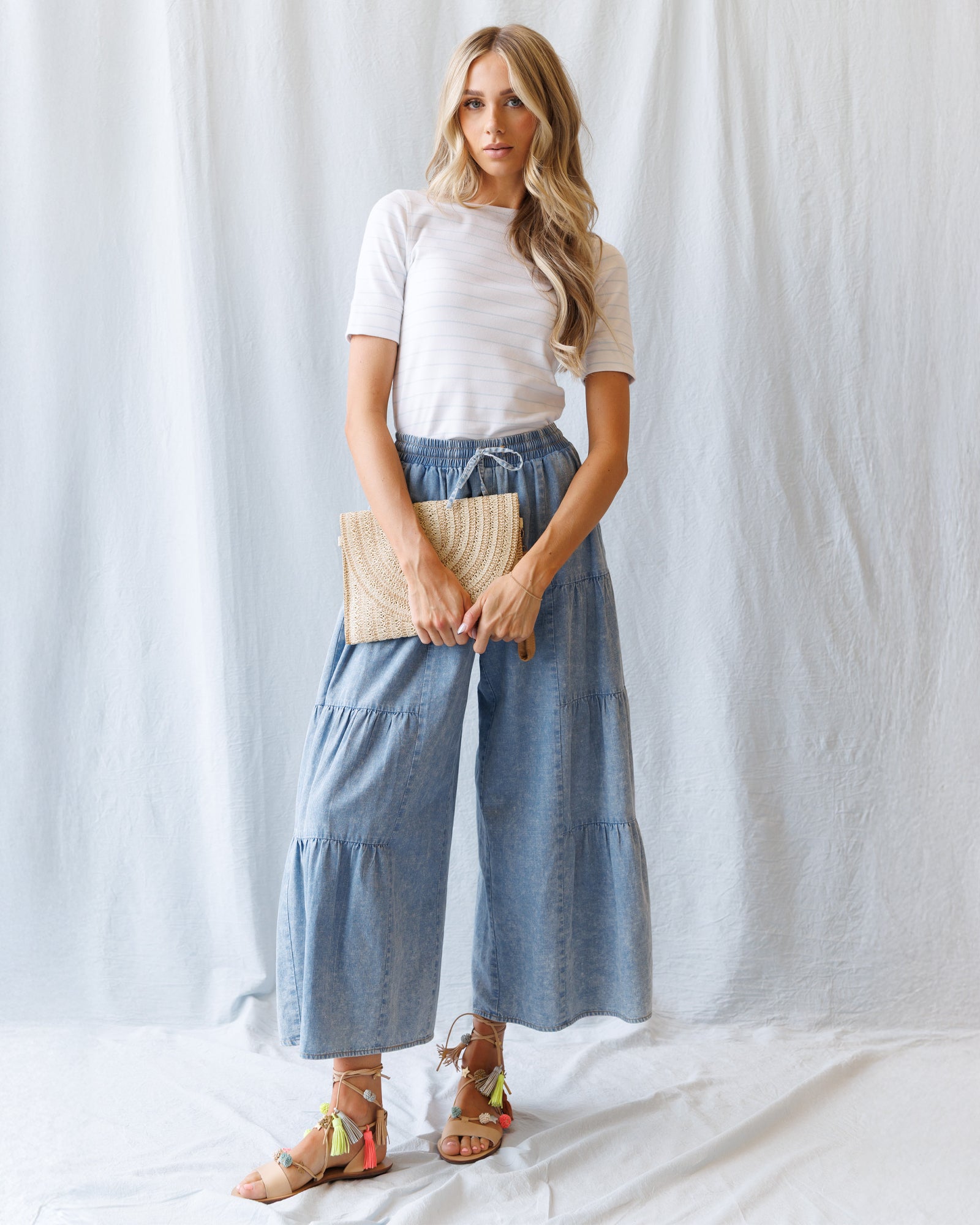Woman standing wearing a white top and blue denim pants against a plain background