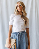 Woman wearing a white t-shirt and blue pants against a plain background