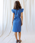 Woman wearing a blue polka dot dress against a white curtain background