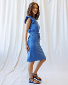 Woman wearing a blue dress with white polka dots against a white curtain background