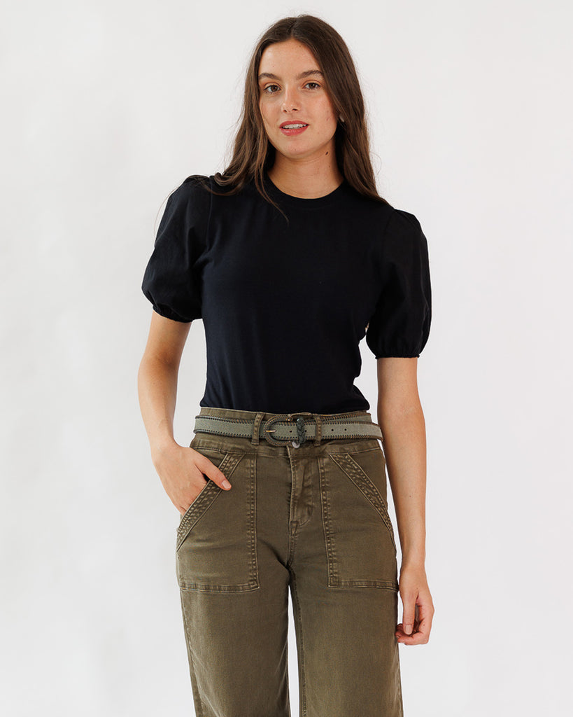 Woman wearing a black top and green pants on a white background