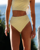 Person wearing a yellow checkered bikini set with a blurred natural background