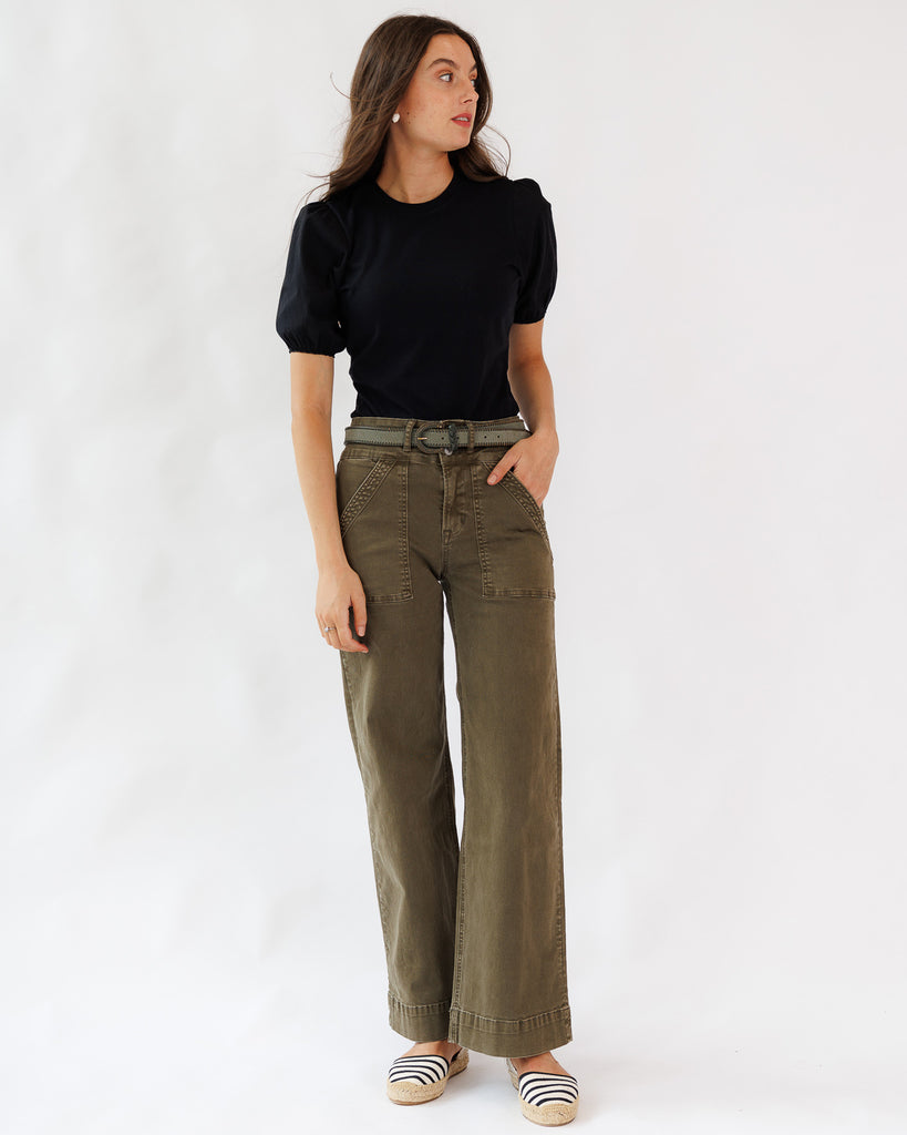 Woman wearing a black top and olive green pants on a white background