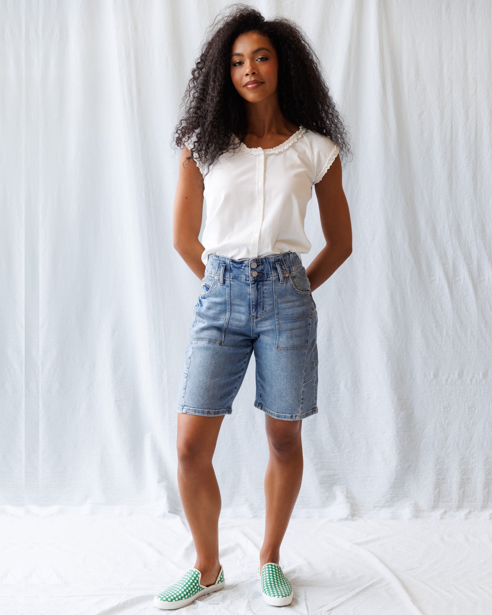 Woman wearing a white blouse and denim shorts against a white background
