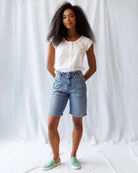 Woman wearing a white blouse and denim shorts against a white background