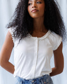 Woman wearing a white blouse with lace details and blue jeans against a light background