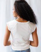Woman wearing a white blouse with lace details on a plain background