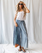 Woman wearing a white polka dot top and blue wide-leg pants against a white background