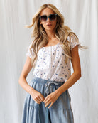 Woman wearing a white floral blouse and blue denim skirt against a light background