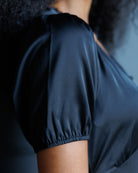 Close-up of a person wearing a dark navy satin-like top with short puff sleeves and a gathered elastic hem.