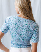 Woman wearing a light blue floral-patterned top against a white background