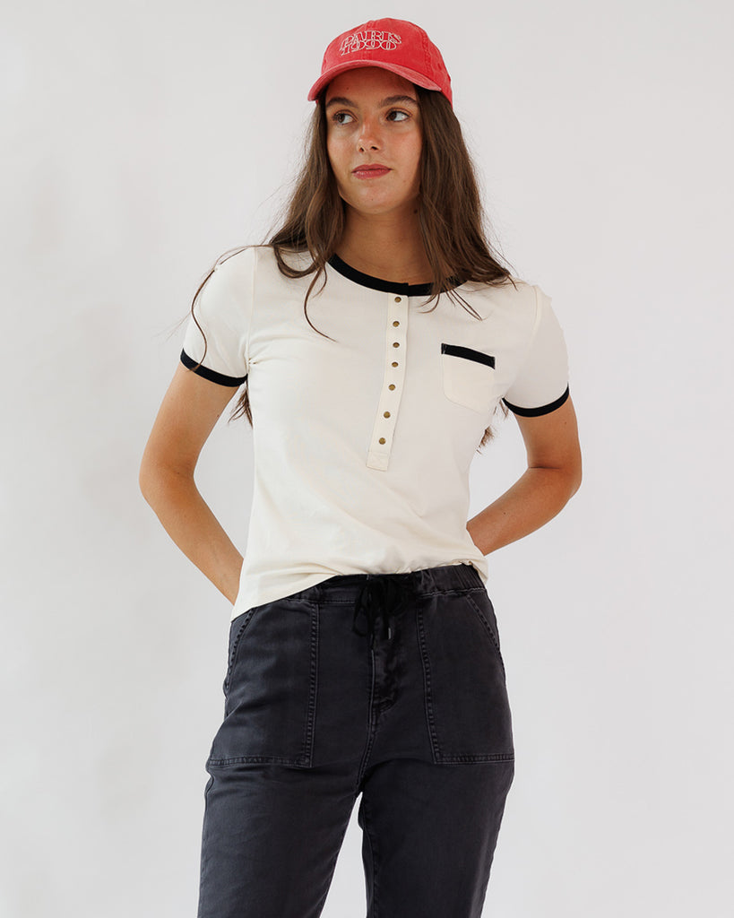 Woman wearing a white shirt with black accents and a red cap on a plain background