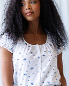 Woman wearing a white blouse with blue floral patterns against a plain background