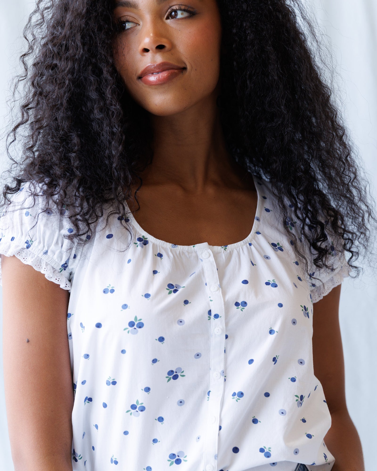 Woman wearing a white blouse with blue floral patterns against a plain background