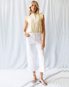 Woman wearing a yellow checkered top and white pants against a white background