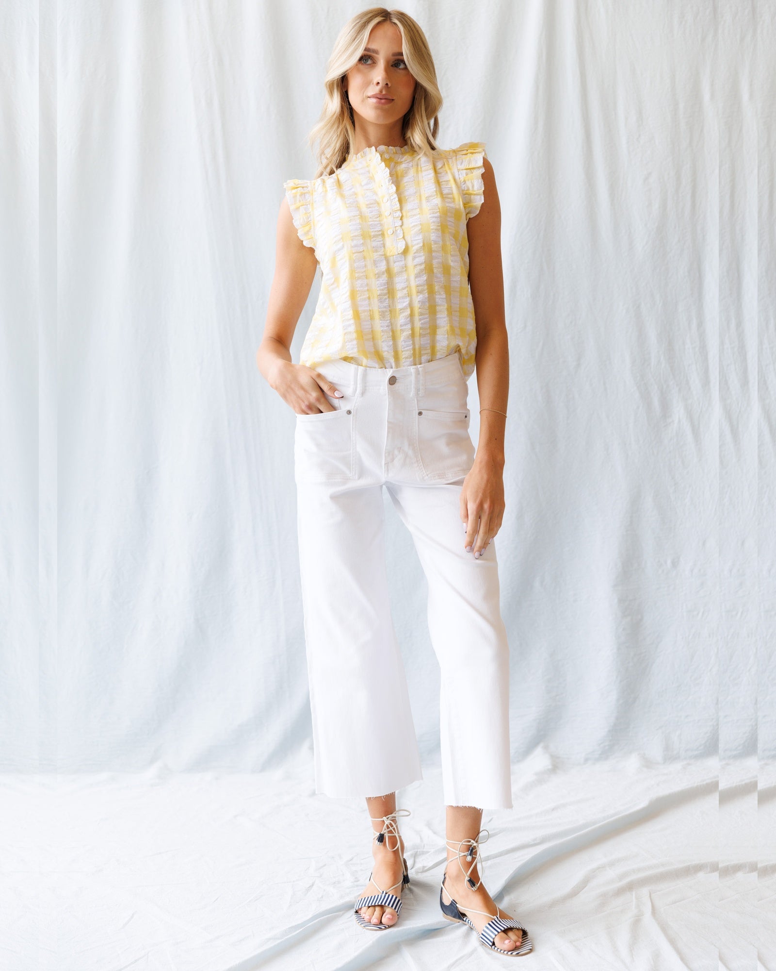 Woman wearing a yellow checkered top and white pants against a white background