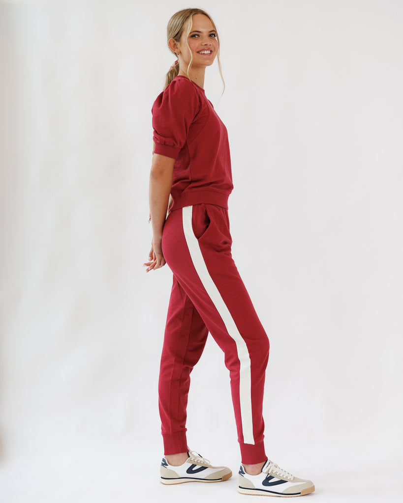 Woman wearing a red jogger matching set with white stripes on a white background