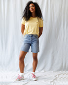 Woman wearing a yellow t-shirt and denim shorts against a white background