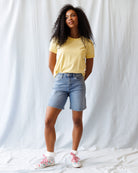 Woman wearing a yellow t-shirt and denim shorts against a white background