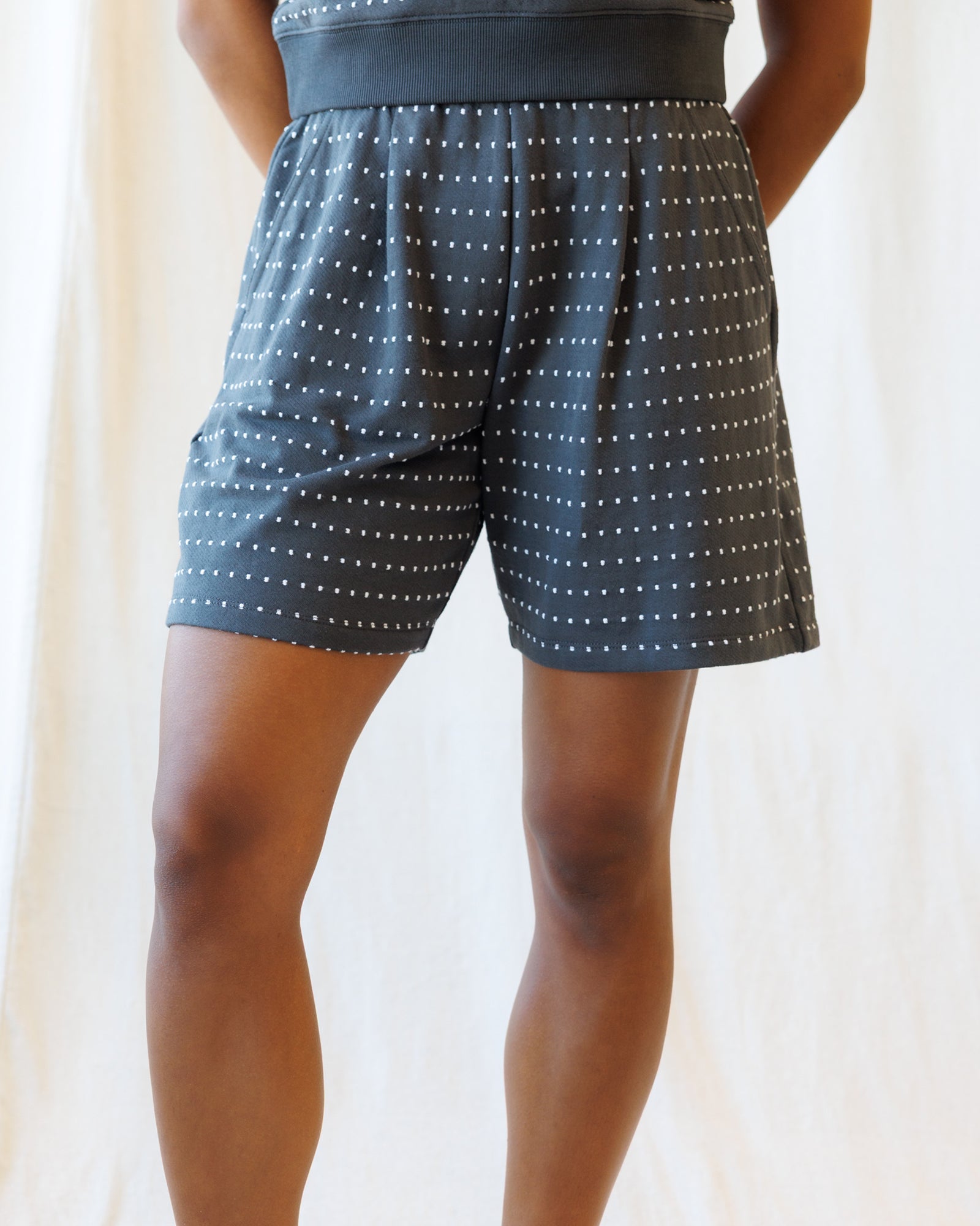 Person wearing black shorts with white pattern on a plain background