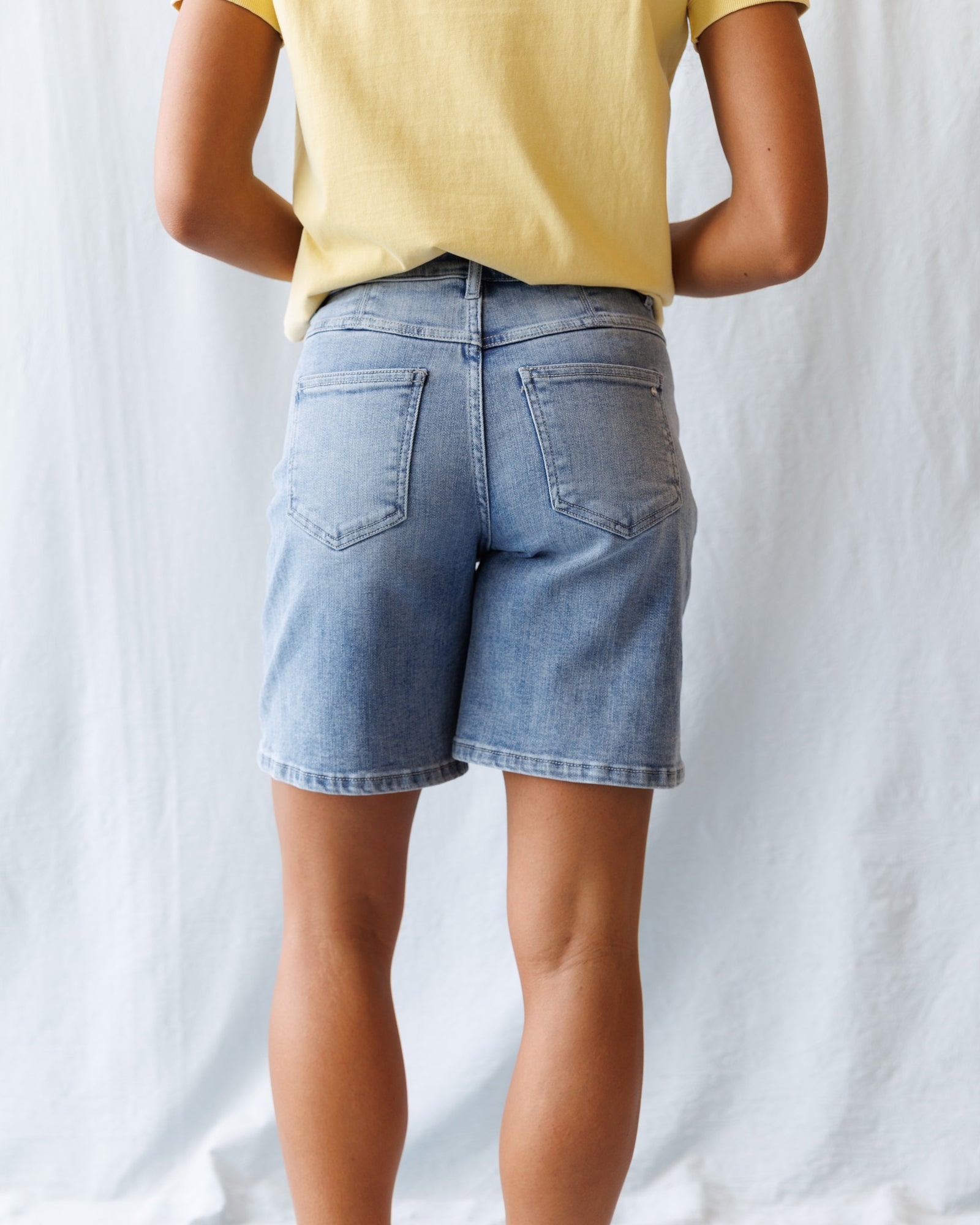 Person wearing a yellow shirt and light blue denim shorts on a white background