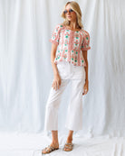 Woman wearing a floral blouse and white pants against a white background