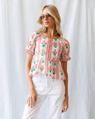 Woman wearing a floral embroidered blouse and sunglasses against a white background