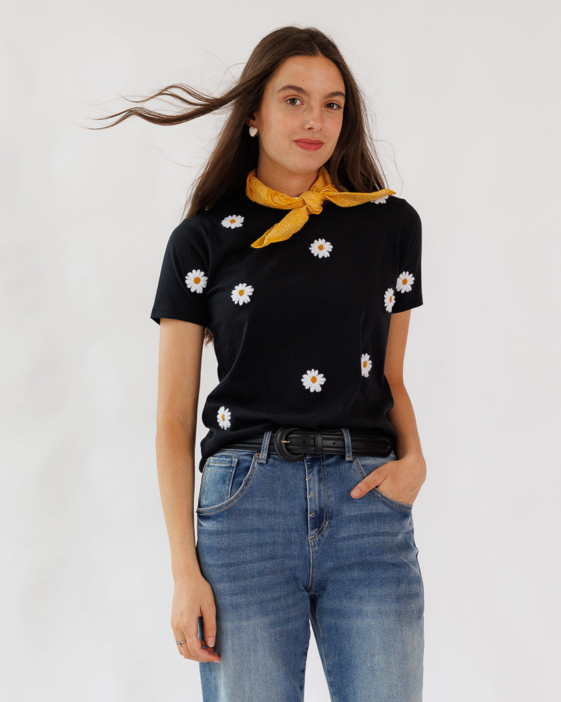 Woman wearing a black t-shirt with white daisy patterns and blue jeans against a white background
