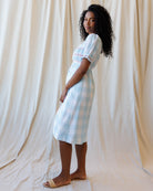 Woman wearing a light blue checkered dress against a beige curtain backdrop